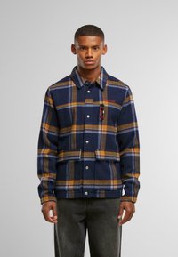 Mørkeblå rutete jakke med oransje og lyseblå striper, med trykknapper, brystlomme med karabinkrok og strukturert design.