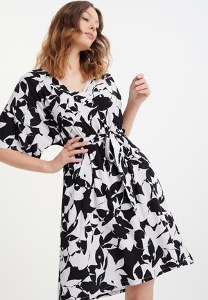 Black and white floral dress with a V-neck, short sleeves, and a drawstring waist, featuring a flowing, lightweight fabric.