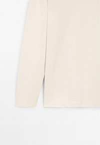 Cremfarbener Langarmshirt mit einfacher, glatter Textur und sauberem Saum vor einem weißen Hintergrund.