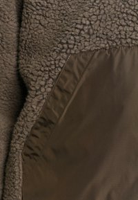 Tissu polaire marron avec laine texturée et panneau en nylon lisse cousus ensemble en gros plan.