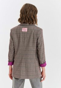 Hnedo-béžové sako s vzorom houndstooth, fialové manžety, priliehavý strih, jeden rozparek a ružová etiketa na zadnej strane. Textúrovaná látka.