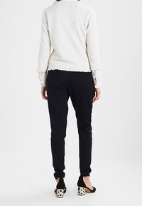 Biały sweter o fakturze z rękawami długości do łokcia, zestawiony z czarnymi spodniami. Czarne baleriny z nakrapianym obcasem dopełniają strój.