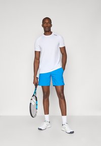 White short-sleeve T-shirt and bright blue shorts. Holding a tennis racket. Textured surface and contrasting colors. Athletic footwear.