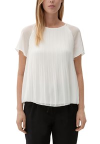 Blouse blanche plissée avec un col rond et des manches courtes, fabriquée dans un tissu léger et lisse, avec une coupe décontractée. Associée à un pantalon noir.