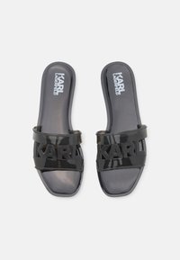 Sandalias de goma negras con una tira ancha que presenta el logo "KARL" de forma prominente. Suela plana con un acabado brillante.