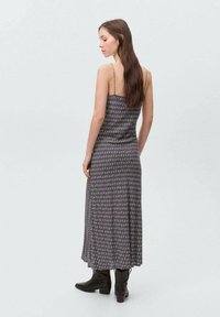 Harmaa kuviollinen maksi-mekko, jossa on ohuet olkaimet, istuva yläosa ja laskostettu hame. Yhdistetty mustiin nilkkureihin, kuvattu takaa.