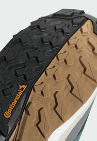 Die schwarze und braune Gummisohle des Sneakers verfügt über multidirektionale Profilierungen für besseren Halt, mit einer strukturierten Oberfläche und dem Continental-Logo in Orange.