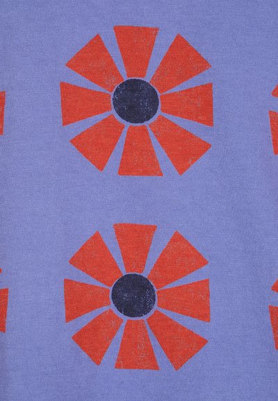 Tela de algodón con fondo lavanda que presenta un patrón repetido de formas de flores rojas y centros negros, texturizada con un acabado ligeramente desgastado.