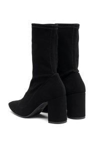 Bottines en tissu noir avec un bout pointu, un talon épais et des détails de couture visibles, présentant une texture lisse et un design ajusté.