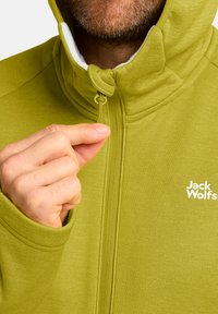 Groene fleece jas met hoge kraag, ritssluiting en een klein logo op de voorkant. Gestructureerde stof en een aansluitende pasvorm. Details op de mouwen.