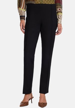 Pantalon noir ajusté porté avec une chemise à manches longues à motifs et des chaussures à talons marron à bride arrière sur un fond uni.