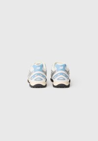 Sneaker con parte superiore in rete bianca, dettagli argento, linguetta sul tallone azzurro chiaro e suola in gomma nera. La vista posteriore mette in evidenza i tagli per la ventilazione.