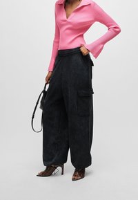 Aansluitende roze geribbelde trui met een v-hals en uitlopende mouwen, gedragen met oversized donkere cargobroeken met zijzakken en een elastische tailleband.