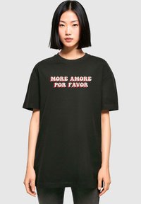 T-shirt in cotone nero con la frase "MORE AMORE POR FAVOR" in caratteri bianchi e rossi, in grassetto e stilizzati. Fit rilassato, maniche corte.