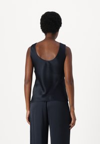 Schwarzes Satin-Top ohne Ärmel mit einem Rundrücken und glatter Textur. Kombiniert mit passenden, gefalteten schwarzen Hosen.