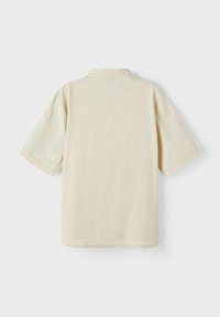 Chemise beige à manches courtes en tissu léger. Elle présente un col classique et une coupe droite avec un design épuré et minimaliste.