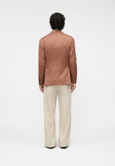 Καφέ-βαγγέρια σακάκι με εφαρμοστή γραμμή, υφασμάτινη υφή και μονή πλαϊνή σχισμή στην πλάτη, συνδυασμένο με ανοιχτό μπεζ παντελόνια φαρδύ πόδι.