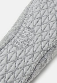 Grå fotbädd med en texturerad vit gummisula. Har ett diamantmönster och en präglad "FALKE"-logotyp. Mjuk yta och böjda kanter.