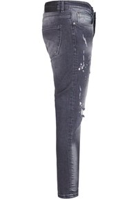 Jeans gris foncé slim avec détails déchirés et éclaboussures de peinture, dotés de poches arrière et de passants pour ceinture, vus de profil.