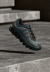 Pantof sportiv gri închis cu accente portocalii, având partea superioară respirabilă, detalii negre și un design unic al tălpii cu amortizare.