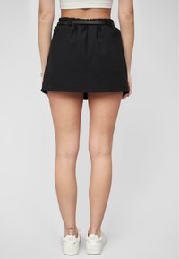 Svarte stoffshorts med elastisk livlinje. Lett materiale, rett snitt, ingen synlige mønstre, kombinert med hvite joggesko.