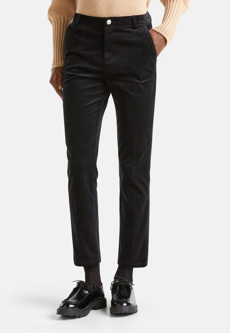 Pantalons en velours côtelé noir avec une coupe slim, dotés de poches avant et d'une fermeture à bouton, associés à des chaussures noires brillantes.
