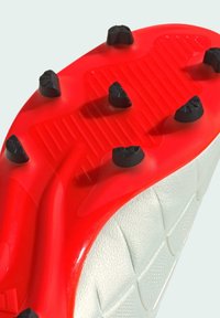 Semelle de crampons de soccer en caoutchouc texturé rouge, avec des crampons noirs pour une traction optimale, et un dessus blanc avec un motif décoratif.
