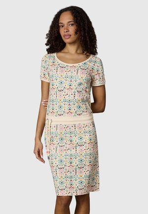 Ung kvinde med krøllet hår iført en kortærmet knælængde kjole med flerfarvet geometrisk mønster og snøring i taljen.