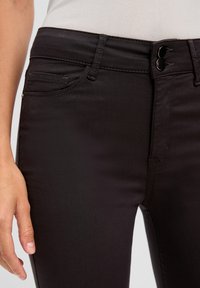 Jean en denim noir à coupe slim, avec une texture lisse, deux poches latérales, une fermeture à double bouton et des détails de couture subtils.