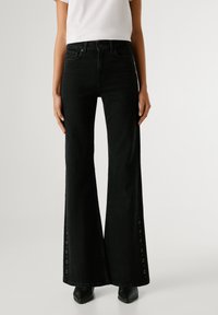 Fekete, magas derekú, oldalsó kivág�ásokkal ellátott farmernadrág, fém grommetekkel rögzítve, klasszikus öt zsebes dizájnnal.