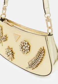 Mała złota torebka z ozdobami w formie kryształowych kwiatów i liści, złotym metalowym wykończeniem oraz zamkiem błyskawicznym na górnej krawędzi.