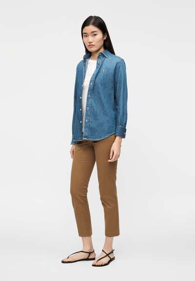 Sinine teksasärk nööpidega, kombineeritud beežide pükstega. Modell kannab all valget T-särki ja musti sandaale.