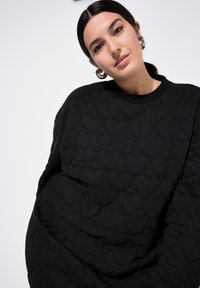 Zwarte gewatteerde sweatshirt met hartvormige patronen, voorzien van een ronde hals en lange mouwen, gemaakt van een gestructureerde stof.