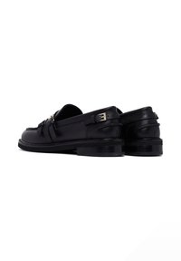 Zwarte leren loafers met een gladde textuur, voorzien van een band en gespsluiting, met een lage hak en een slank ontwerp.