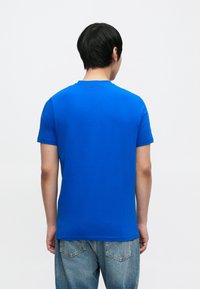 Ķiršu zilas krāsas īsroku T-krekls ar apaļu kaklu, izgatavots no kokvilnas, ar gludu tekstūru un vienkāršu dizainu bez redzamām rakstu zīmēm.