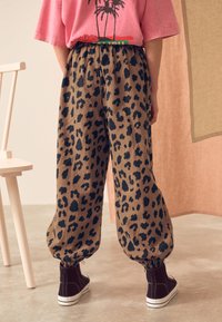 Brown leopard print pants with elastic cuffs, paired with black sneakers. The fabric has a textured appearance, offering a relaxed fit.
