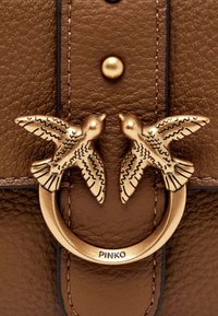 Sac à main en cuir marron avec un fermoir en métal doré proéminent orné de deux oiseaux stylisés. Clous décoratifs sur le devant.