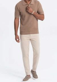 Polo à manches courtes tan en maille texturée, assorti à un pantalon beige clair coupe slim et des chaussures à enfiler marron clair. Accessoire bracelet marron.