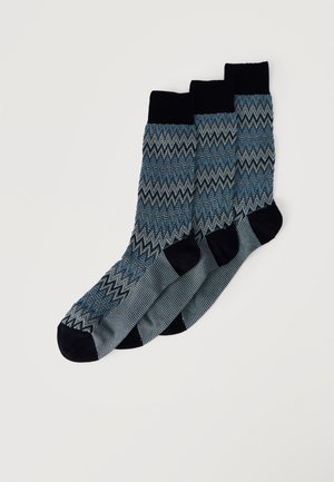 Tres pares de calcetines hasta la mitad de la pantorrilla con puños, talones y punteras negros, con un patrón de zigzag en azul, negro y gris en el cuerpo principal.
