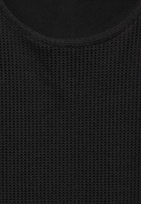 Tela negra texturizada con un patrón de malla, con un escote redondeado y costuras visibles a lo largo de los bordes.