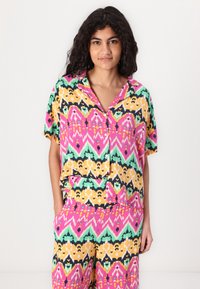 Top a maniche corte con colletto e pantaloni abbinati in un vivace motivo ikat multicolore. Presenta forme rosa, gialle, verdi e blu scuro; tessuto leggero.