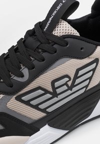 Zwarte en beige sport sneaker met mesh stof, geprofileerde leren accenten, prominent logo in zilver en zwarte veters.