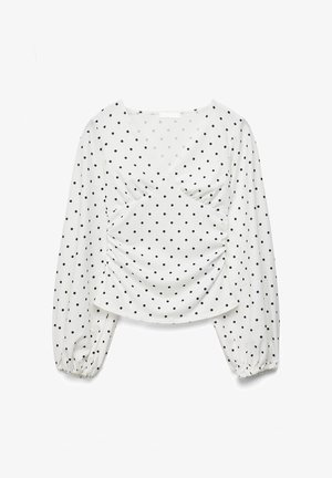 Blusa bianca a maniche lunghe con pois neri, scollo a V, davanti arricciato e polsini elasticizzati sulle maniche.