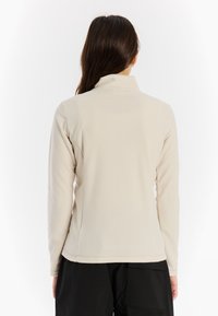 Helles beiges Fleece-Jacke mit hohem Kragen, langen Ärmeln und glatter Textur. Sie bietet eine lockere Passform mit einem leicht geschwungenen Saum.