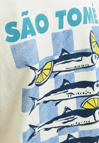 Katoenen T-shirt met een graphic van vissen met schijfjes citroen op een blauw-wit geblokt patroon. Tekst leest "SÃO TOMÉ".