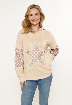 Hanorac bej cu un model mare de stea într-un pattern floral. Are o glugă cu șnur și mâneci lungi cu manșete elastice.