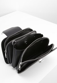 Černá kožená kabelka s texturovaným povrchem, se třemi zipovými oddíly a stříbrnými kovovými prvky. Kompaktní a přehledný design.