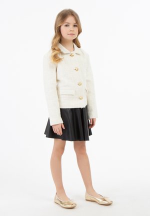 Weiße strukturierte Jacke mit goldenen Knöpfen, schwarzer gefalteter Rock und metallisch goldene Ballerinas, ausgestattet mit einem klassischen Kragen und langen Ärmeln.