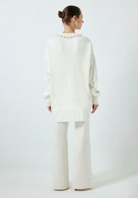 Valge ülikas suurus-sweater, millel on soonikkoes mansetid ja äär, kaunistatud kaeluse servaga. Koos sobituvate kreemjat tooni laienevate pükstega.