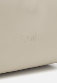 Beige vanntett bag laget av matte materialer, med preget "RAINS"-logo. Enkel design uten synlig maskinvare eller mønstre.